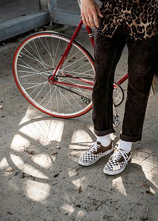 Persona apoyandose en una bicicleta con zapatillas vans y ropa casual 